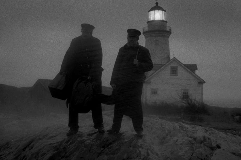 Image of two lighthouse keepers standing on a dune in front of the lighthouse in a black and white image