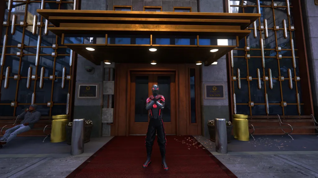 An image showing Miles Morales in front of the Wakandan Embassy doing the Wakandan salute. He's wearing his Wakanda-style suit. The picture is part of an article listing all the suits for Miles Morales in Marvel's Spider-Man 2 and how to unlock them.