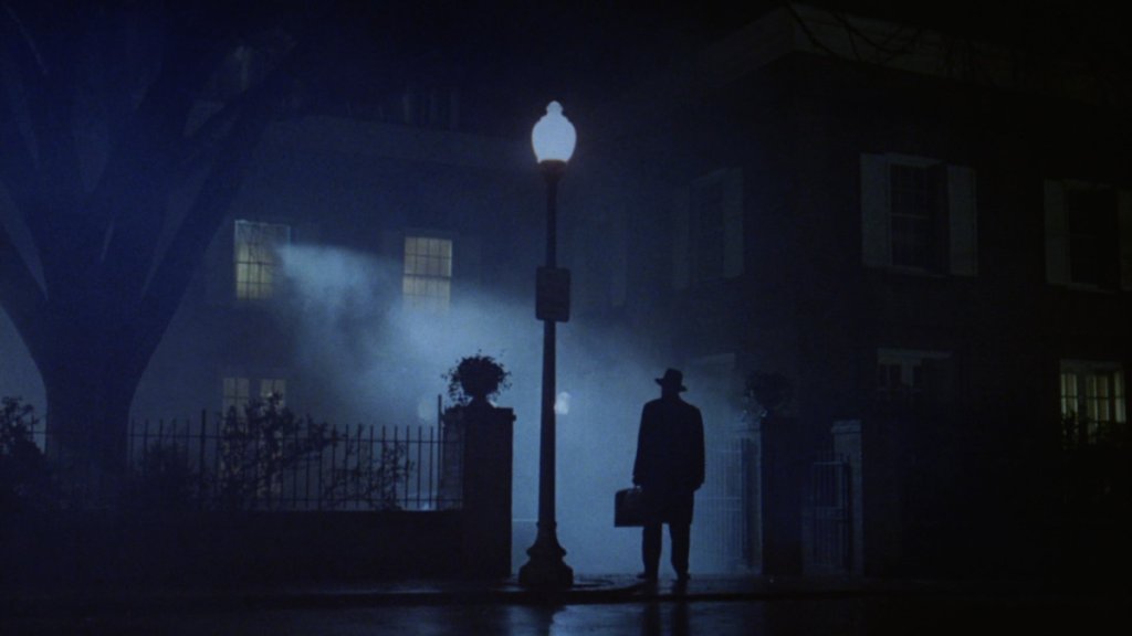 Father Merrin stands outside of the MacNeill household in the fog as part of an article about the best horror movies on streaming.