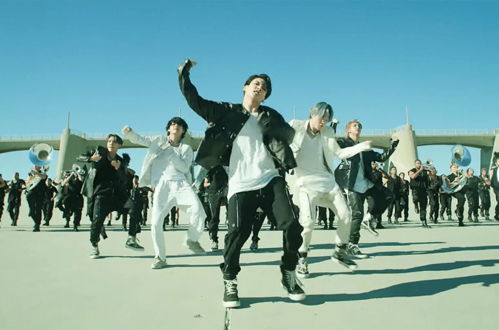 BTS dance in front of a bridge with a marching band