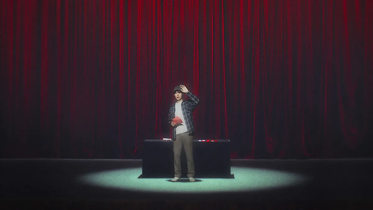 A man standing on a stage in front of a table, holding a red envelope and looking at the audience in The 8 Show. 