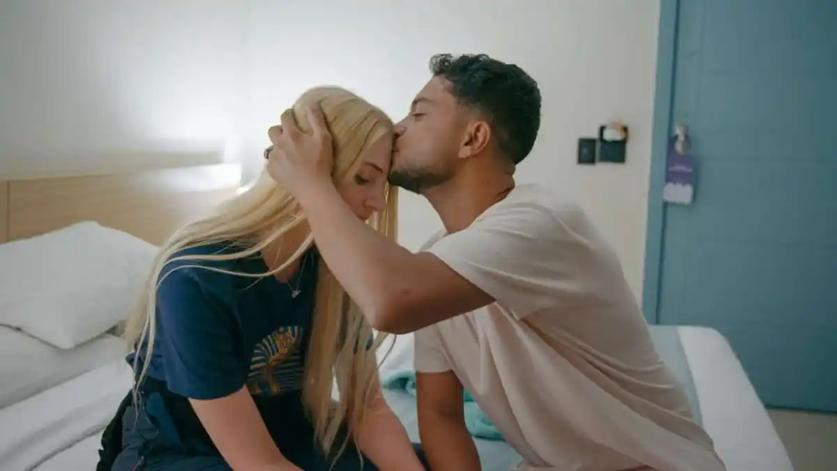 A man kissing a blonde woman's head, sitting on a bed, in 90 Day Fiance UK. 