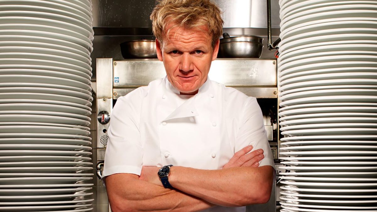 Gordon Ramsay from Kitchen Nightmares standing between two huge stacks of plates, with his arms crossed