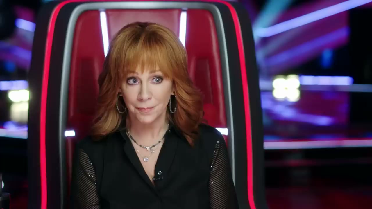 Reba McIntyre in The Voice, sitting on one of the red chairs.