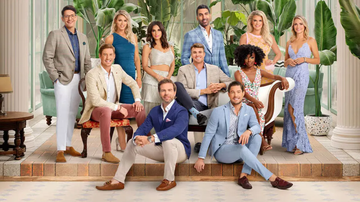 The cast of Southern Charm, smiling and sitting on and standing around a sofa. 