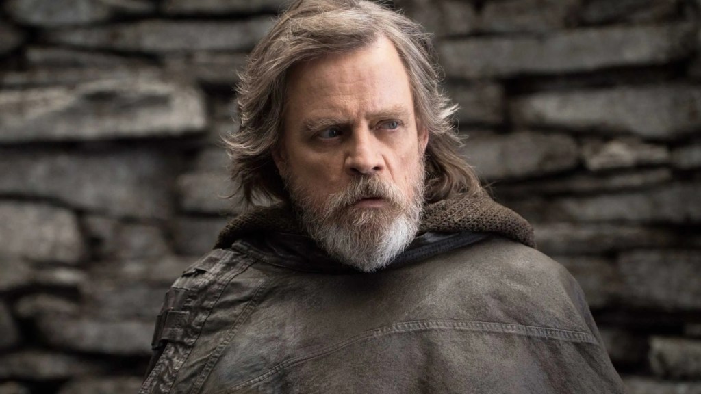 Luke Skywalker in Star Wars: The Last Jedi looking grizzled and jaded, dressed in a leather smock, frowns at someone off screen