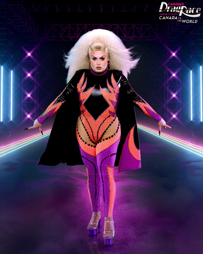 Cheryl Hole posing like Storm in a leather-esque cape and leotard with orange and purple accents on a stage 