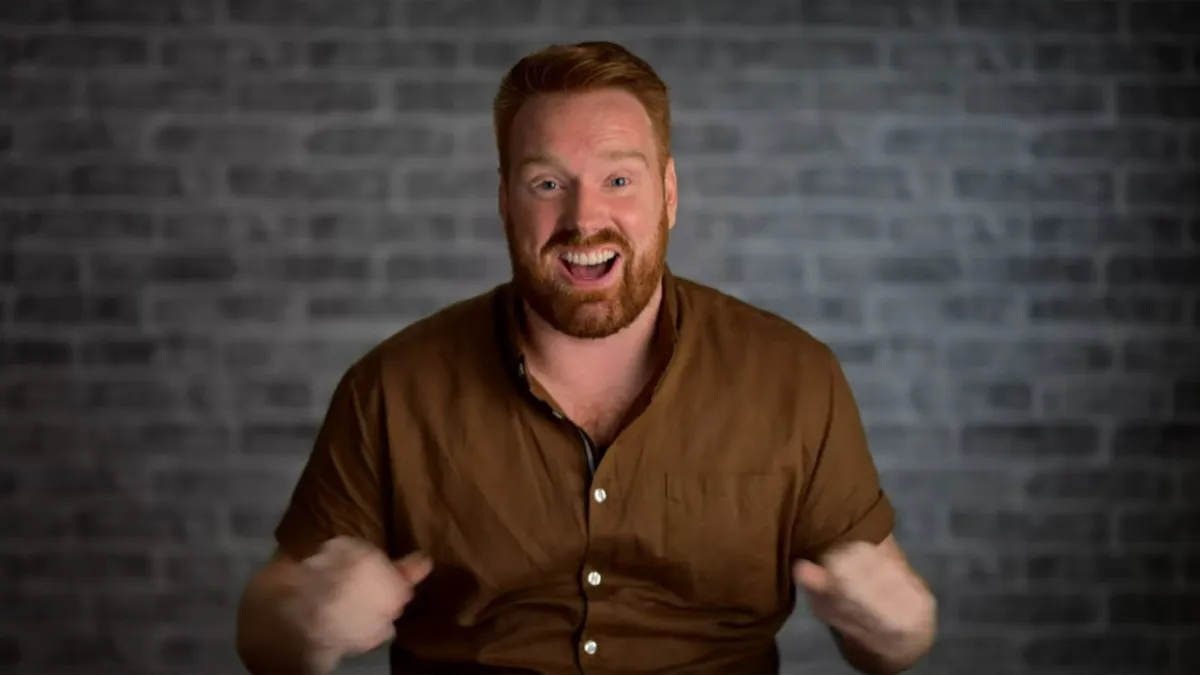 Michael from The Mole Season 2, a red-headed man, with a beard and a brown shirt. 