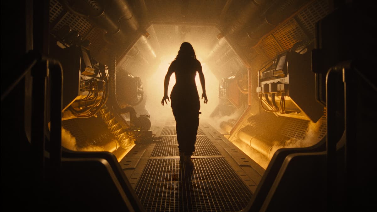 A scene from Alien: Romulus which depicts the character Kay (Isabela Merced) walking down a tunnel of a spaceship