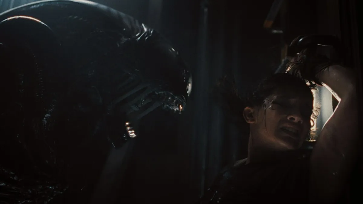 A Xenomorph getting close up to Rain as she shrinks away in Alien: Romulus