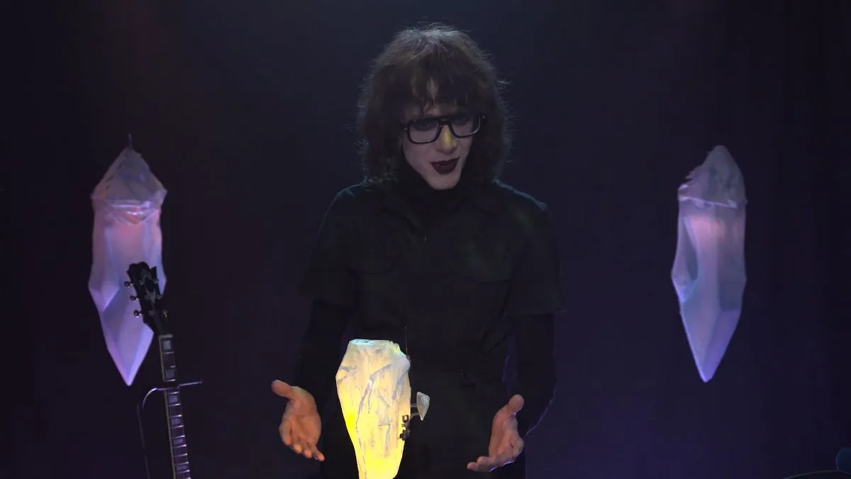 Image of a person surrounded by floating crystals, dressed in black and goth style makeup in Critical Role's Moonward