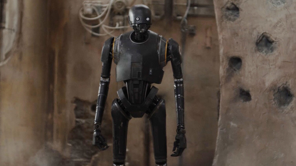 K-2SO on Jedha in Rogue One: A Star Wars Story, standing in a bullet-riddled town staring off screen