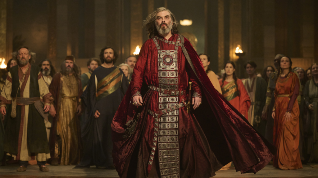 Pharazon in The Lord of the Rings: The Rings of Power Season 2, standing in red robes in a large room with a group of people behind him