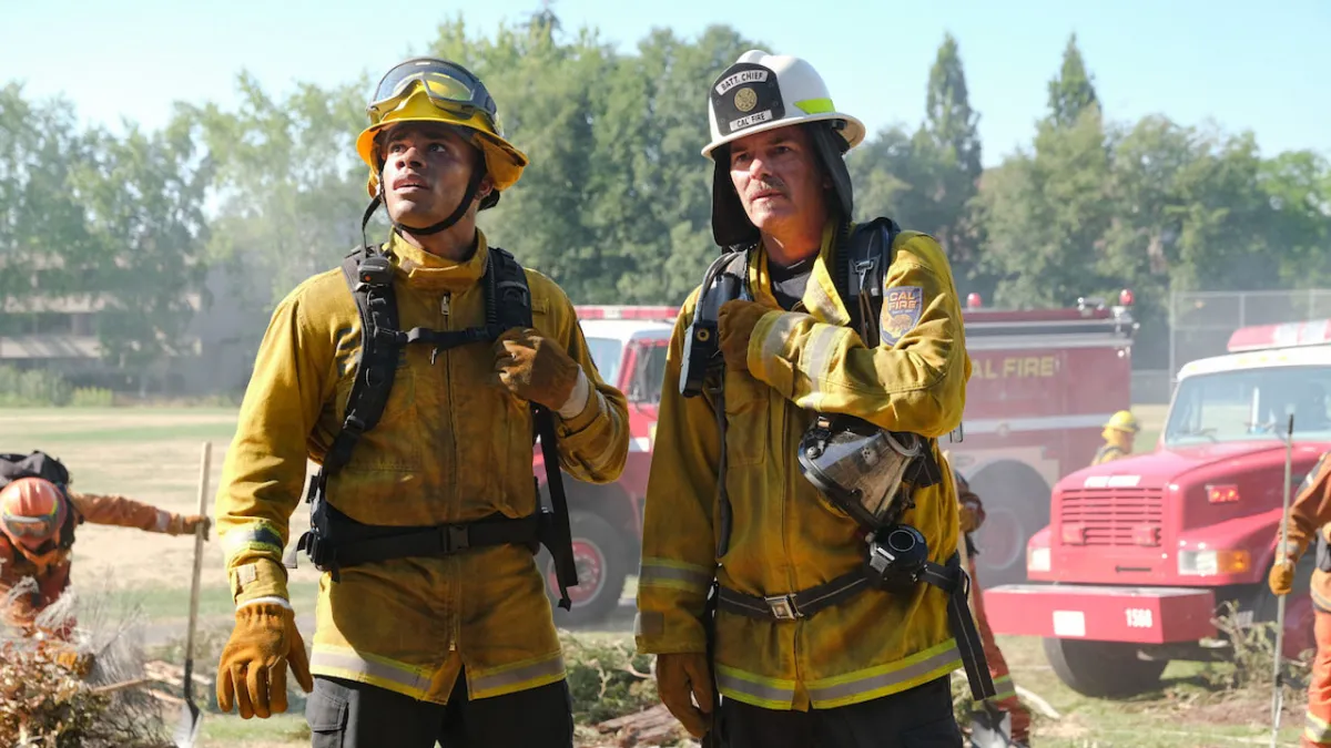 Two firefighters in Fire Country, standing in front of trucks, light smoke around them as part of an article about whether Fire Country has a Season 2 release date on Netflix.