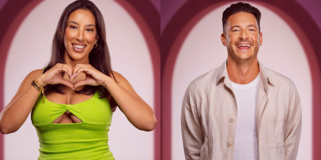 Tom and Maria stand beside together on a pink background in casual clothes while Maria makes the shape of a heart with her hands 