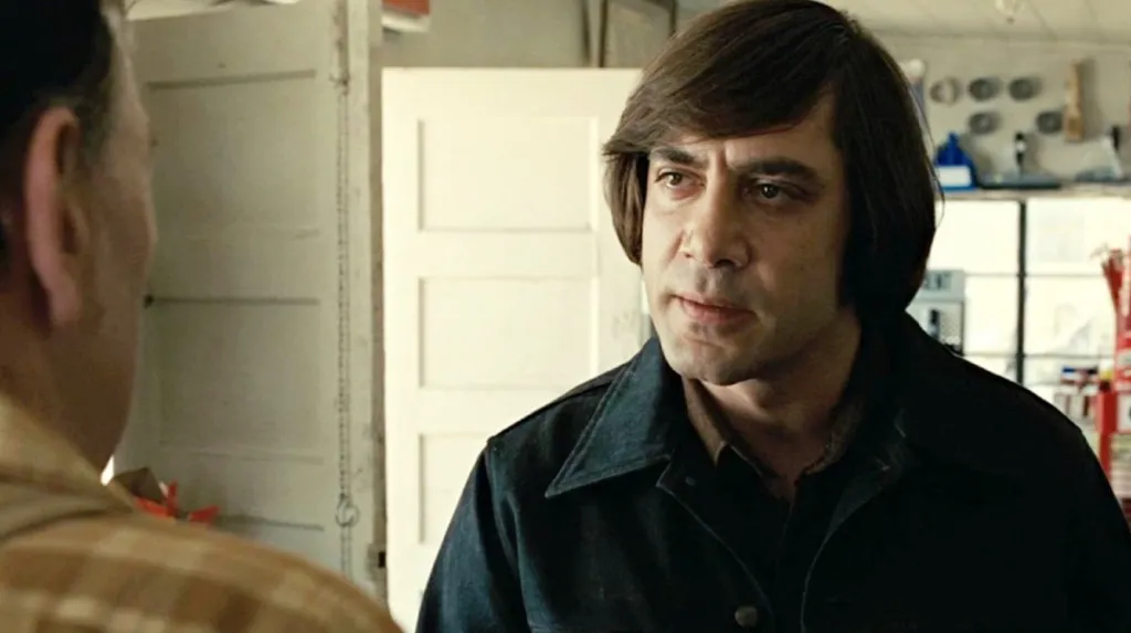 Anton speaks with an attendant with a serious look on his face in No Country for Old Men