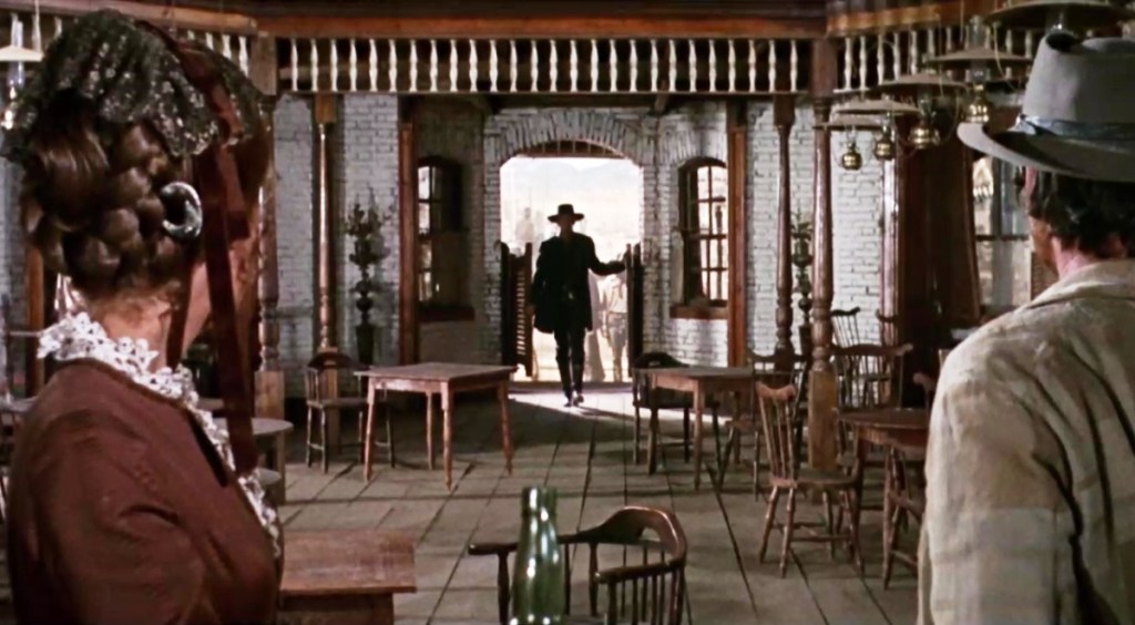 Frank enters the saloon as Harmonica watches