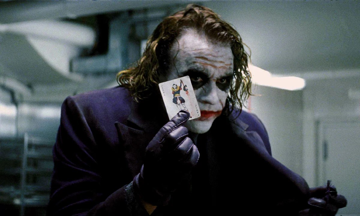 Heath Ledger as the joker holding up a Joker card in the dark knight