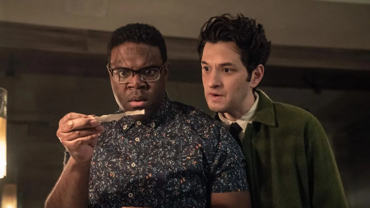 Two men stare apprehensively at a strip of torn paper held by the man closest to the camera who seems to have the word 'NERD' imposed over his forehead