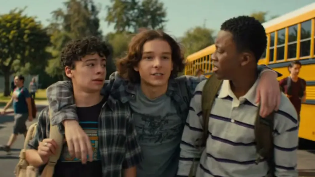 A boy tosses his arms around two other reluctant students outside of a line of school buses in Incoming