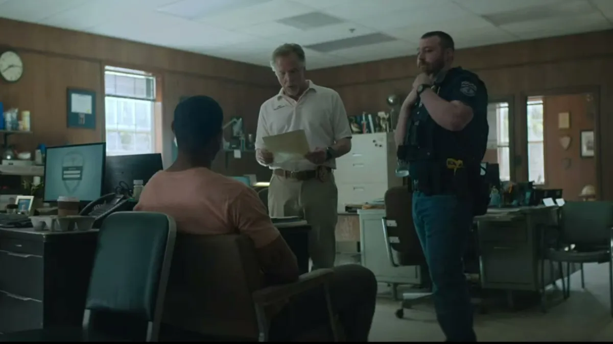 Terry Richmond in Rebel Ridge, seated, with the sheriff and a cop standing. 