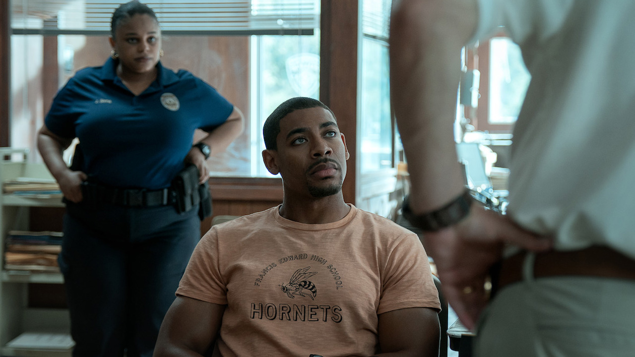 Rebel Ridge, Terry sitting in the police station with the chief of police looking down on him.