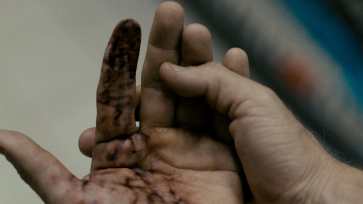 Someone examining and holding their hand in Splinter. Their first finger and part of the hand is greying as part of an article about the 10 best body horror movies.