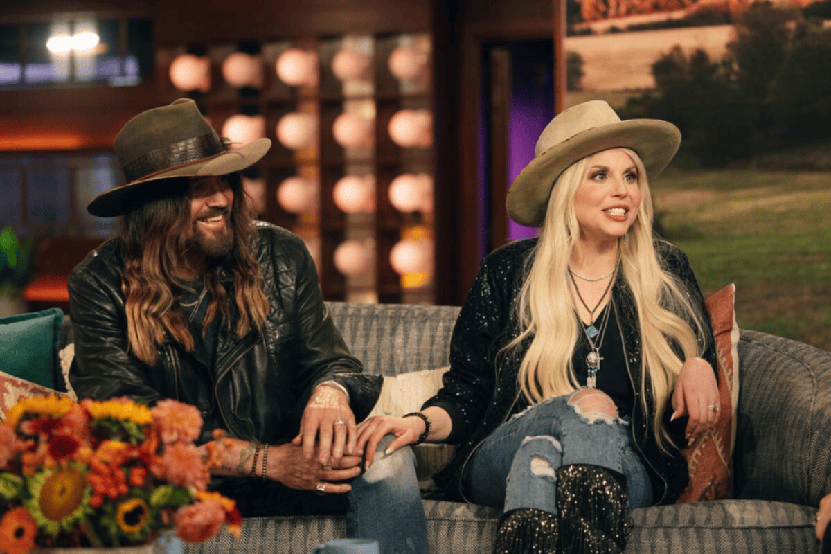 Billy Ray Cyrus and Firerose on a talk show, laughing together as part of an article about celebrity divorces.